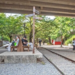 高架下に線路跡が残る京義線森の道公園。旧西江駅のホームを模した台の上にベンチが置かれ、案内標識の先を通行人が歩いている