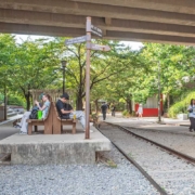 高架下に線路跡が残る京義線森の道公園。旧西江駅のホームを模した台の上にベンチが置かれ、案内標識の先を通行人が歩いている