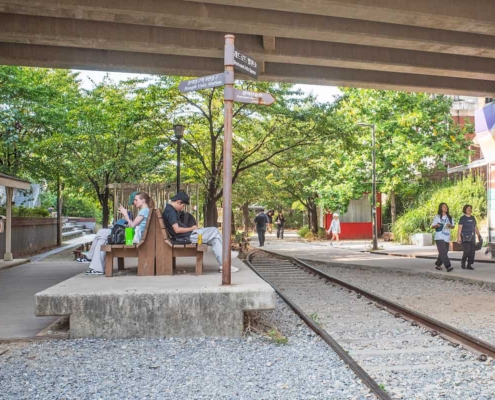 高架下に線路跡が残る京義線森の道公園。旧西江駅のホームを模した台の上にベンチが置かれ、案内標識の先を通行人が歩いている